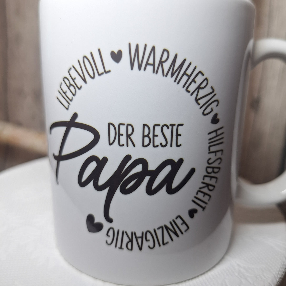 Nahaufnahme des Aufdrucks „Der beste Papa“, umrahmt von liebevoll, warmherzig, hilfsbereit und einzigartig sowie Herzen.