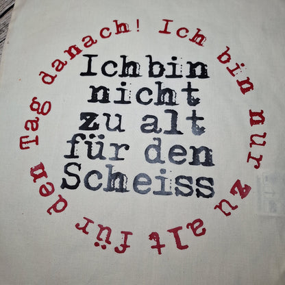 Nahaufnahme des schwarzen Schriftzugs mit kreisförmig angeordnetem rotem Text auf der naturfarbenen Stofftasche.
