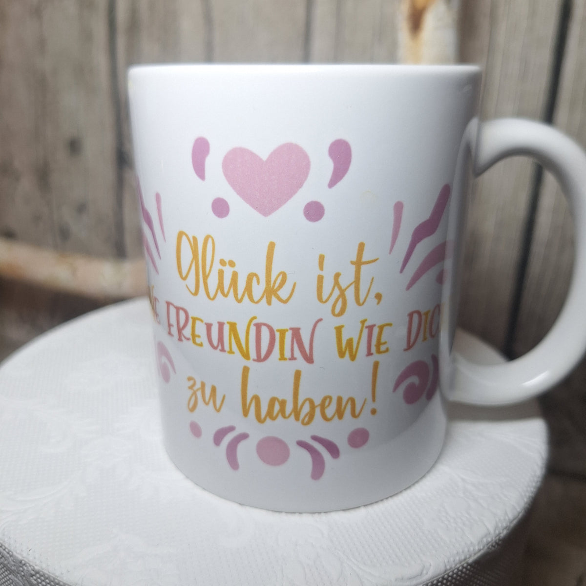 Weiße Tasse mit „Glück ist, eine Freundin wie dich zu haben!“ in Gelb und Rosa, mit rosa Herz.