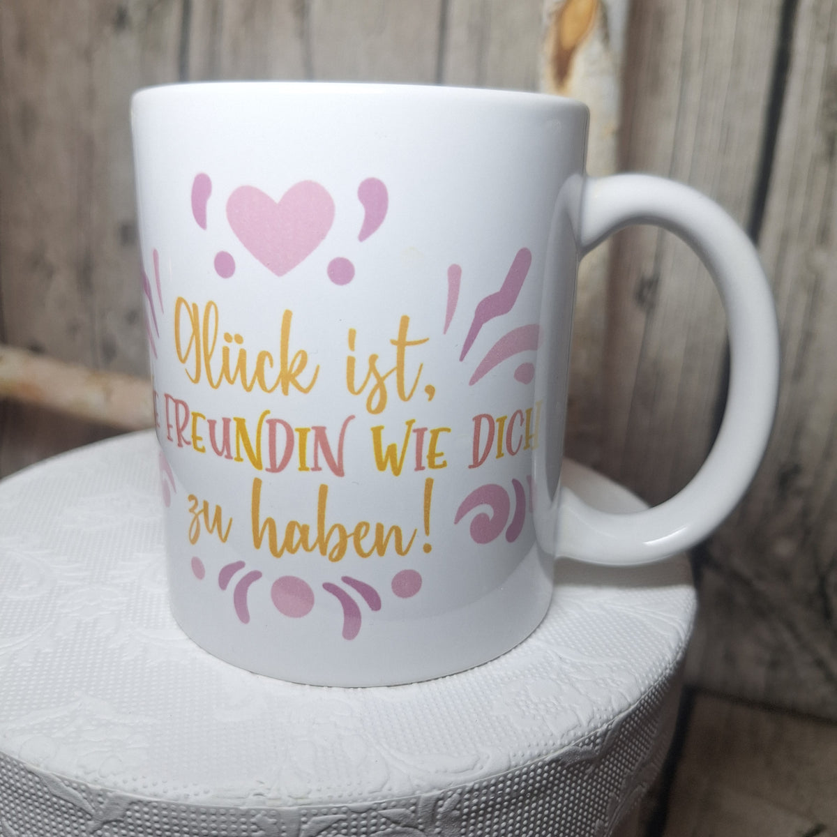 Weiße Keramiktasse mit Freundschaftsspruch, rosa Herz und gelb-rosa Schrift in leicht gedrehter Ansicht.