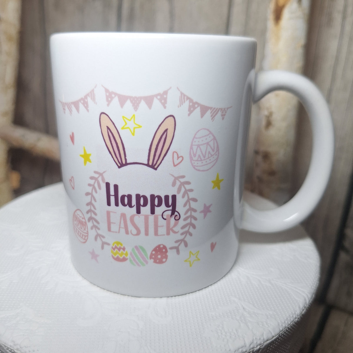 Weiße Ostertasse mit „Happy Easter“, Hasenohren, Ostereiern und Wimpelkette in Pastellfarben, Henkel rechts.