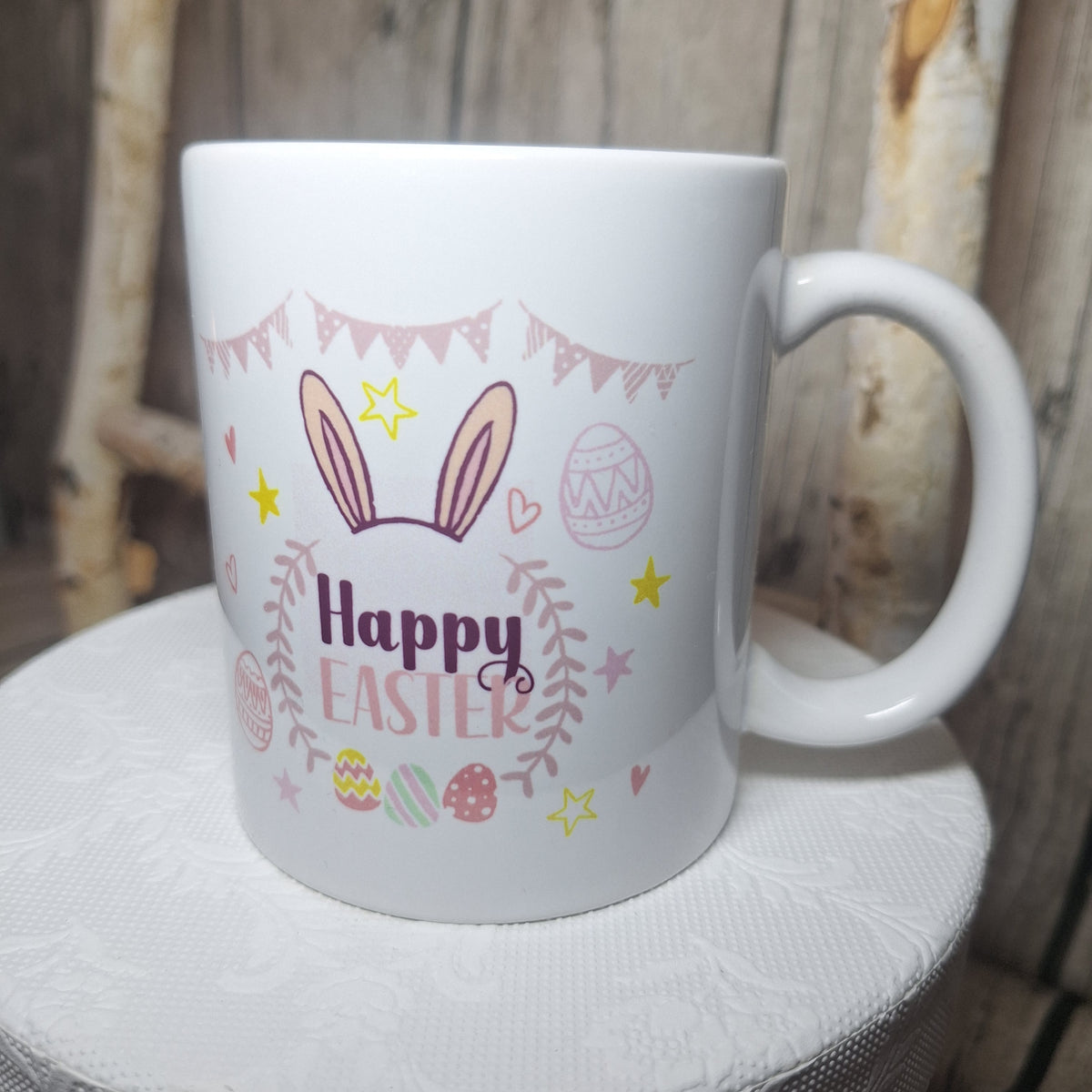 Weiße „Happy Easter“-Tasse mit pastellfarbenen Ostermotiven, gelben Sternen und sichtbarem Henkel rechts.