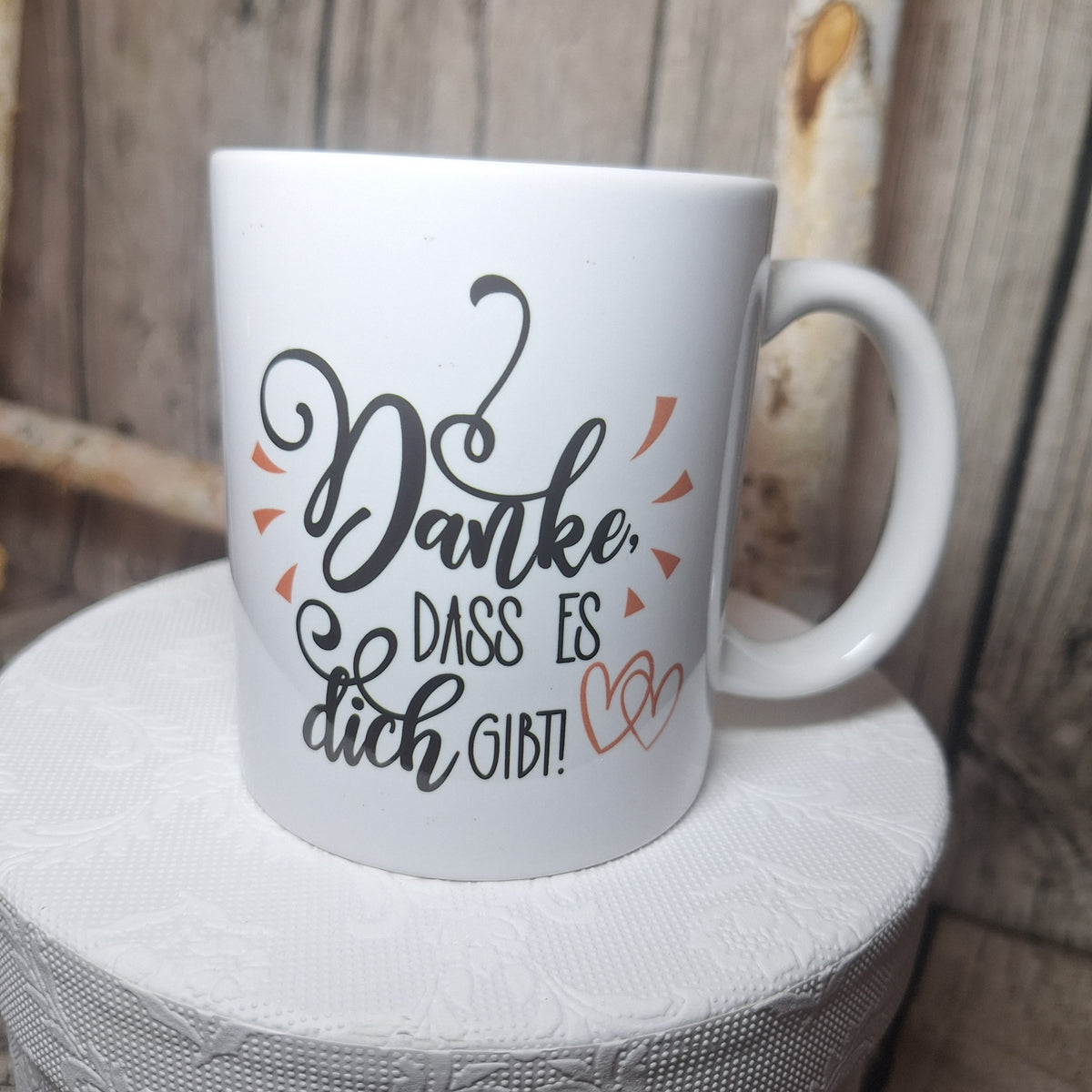 Weiße Dankeschön-Tasse in leicht gedrehter Ansicht mit schwarzem Schriftzug und zwei lachsfarbenen Herzen.