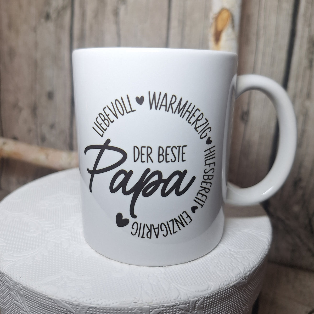 Weiße Keramiktasse mit schwarzem Schriftzug „Der beste Papa“, Herzmotiven und kreisförmig angeordneten Eigenschaften.
