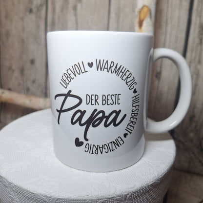 Weiße Keramiktasse mit schwarzem Schriftzug „Der beste Papa“, Herzmotiven und kreisförmig angeordneten Eigenschaften.