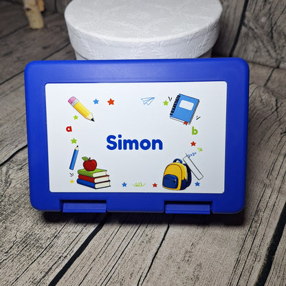 Blaue Brotzeitbox mit dem Namen Simon und bunten Schulmotiven auf dem Deckel.