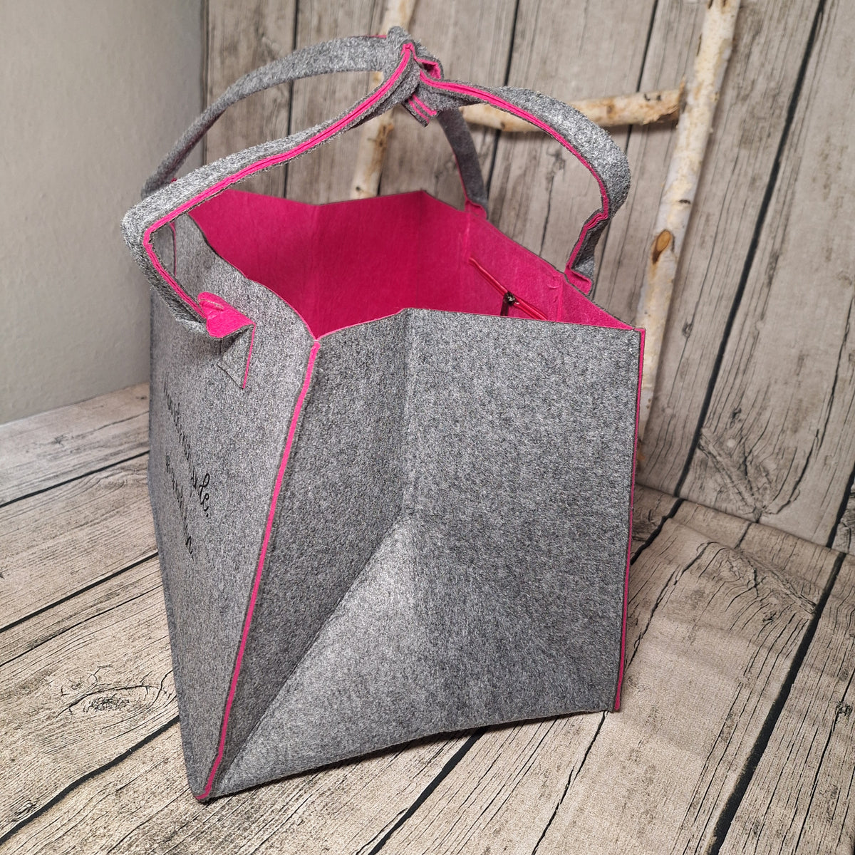 Seitenansicht der grauen Filztasche mit breitem Boden, pinker Innenseite und zusammengehaltenen Tragegriffen.