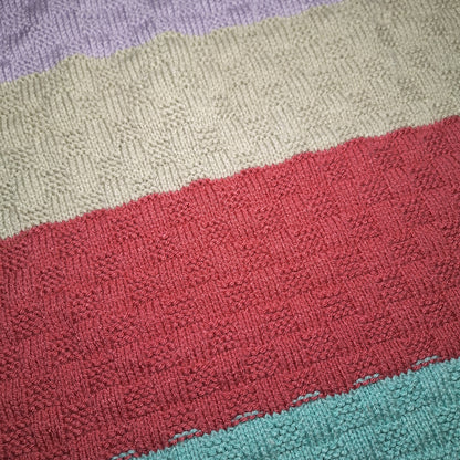 Nahaufnahme der Babydecke mit strukturiertem Strickmuster in Flieder, Grau, Beerenrot und Türkis.