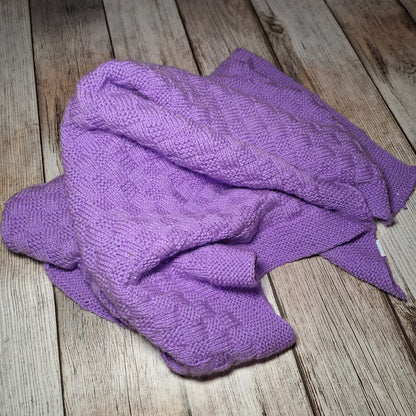 Locker in Falten gelegte fliederfarbene Strickdecke mit sichtbarem Strukturmuster und gestricktem Rand.