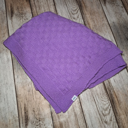 Zusammengelegte Babydecke in Flieder mit Strukturmuster, breiter Bordüre und kleinem Markenetikett.