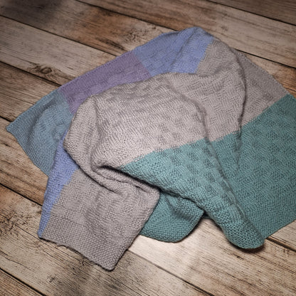 Locker in Falten gelegte Babydecke mit breiten Pastellstreifen, Strukturmuster und gestricktem Rand.