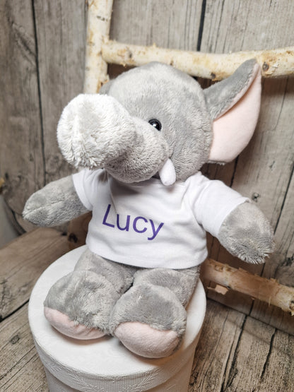 Grauer Plüschelefant mit weißem T-Shirt und dem Namen Lucy in violetter Schrift.
